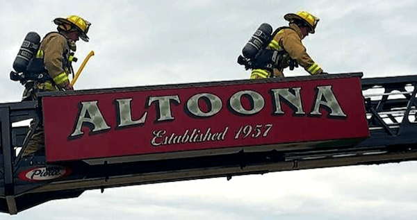 Photo of two firefighters on a structure above a sign for the City of Altoona.