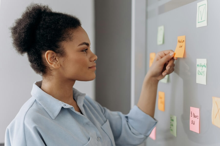 Image of a woman placing colorful post-it notes on a whiteboard as part of a strategic planning process.