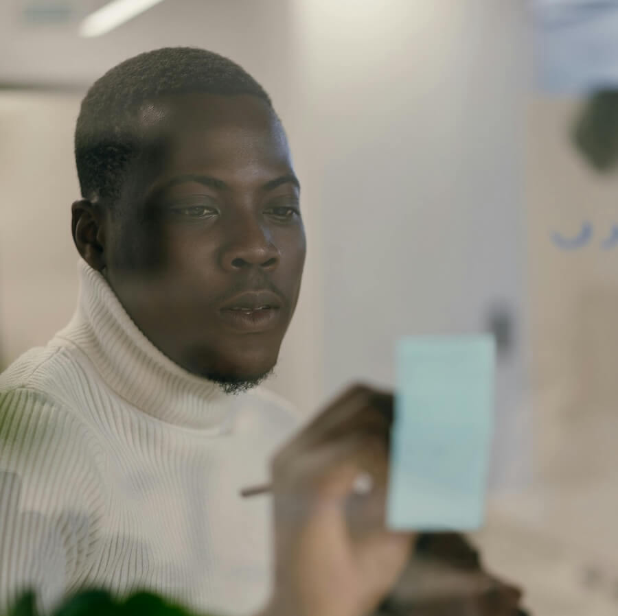 Photo of a man writing on a post-it note on a glass wall.
