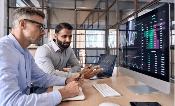 Photo of two men sitting at a desk and discussing something on a computer monitor.