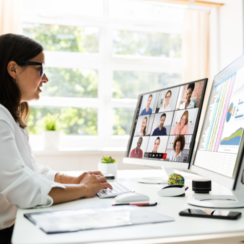 Woman at her desk in a bright office watching a webinar on two screens