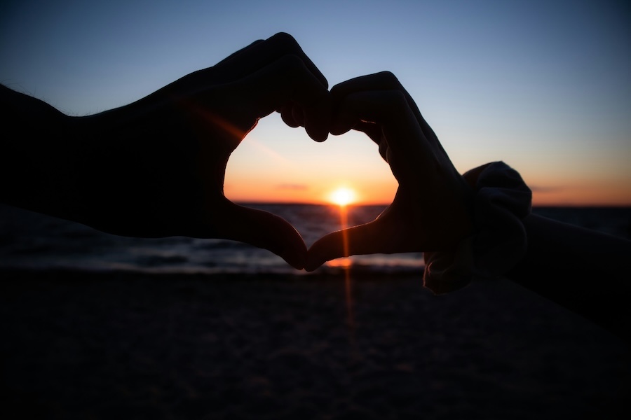 Photo of two hands making a heart shape at sunset to show trust.