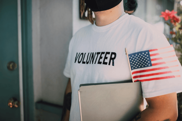 A man wearing a white shirt with writing, "Volunteer", with a small American flag tucked in his arm